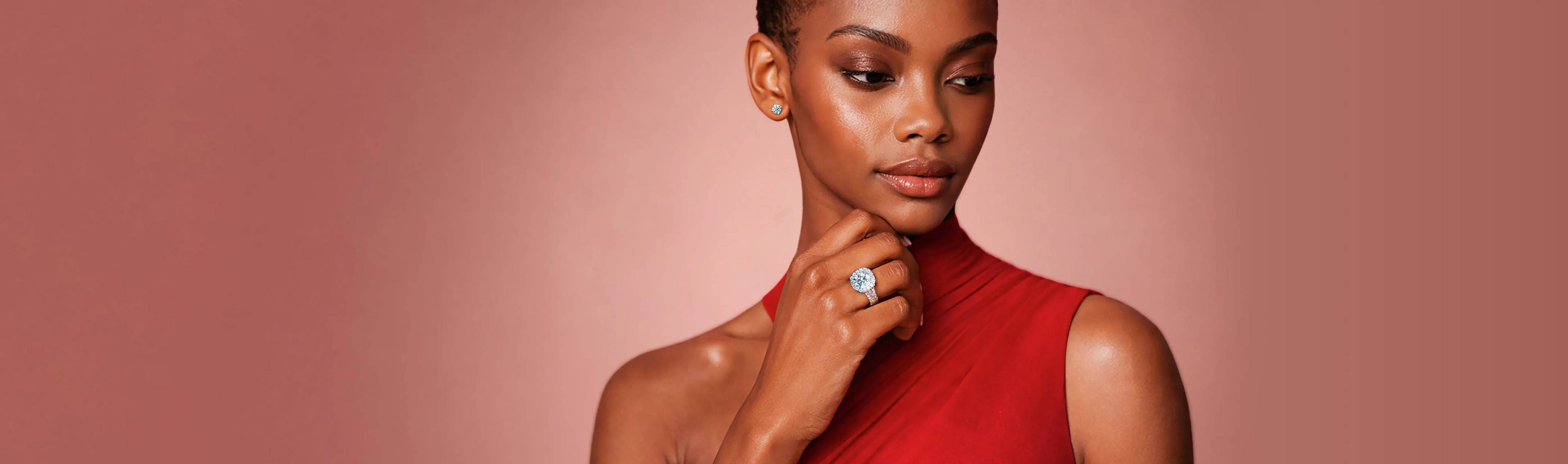 Model on a peachy pink background wearing a cushion halo engagement ring with a round cut diamond