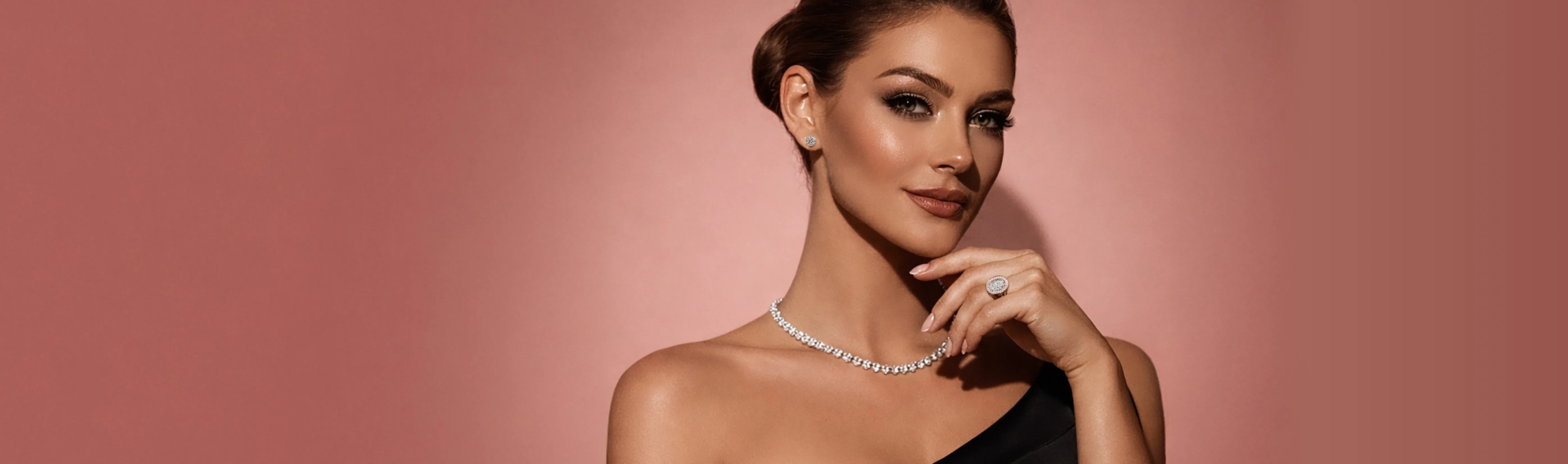 Model on a peachy pink background wearing a cushion halo engagement ring with a round cut diamond and tennis necklace